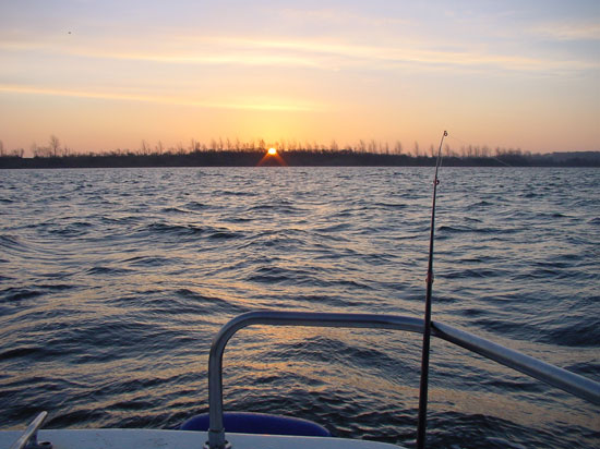 Sonnenaufgang über dem Wasser, vom Boot mit Blick aufs Land aus fotografiert