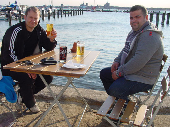 Angler Jan und Tuncay am Tisch im Hafen, im Hintergrund das Wasser